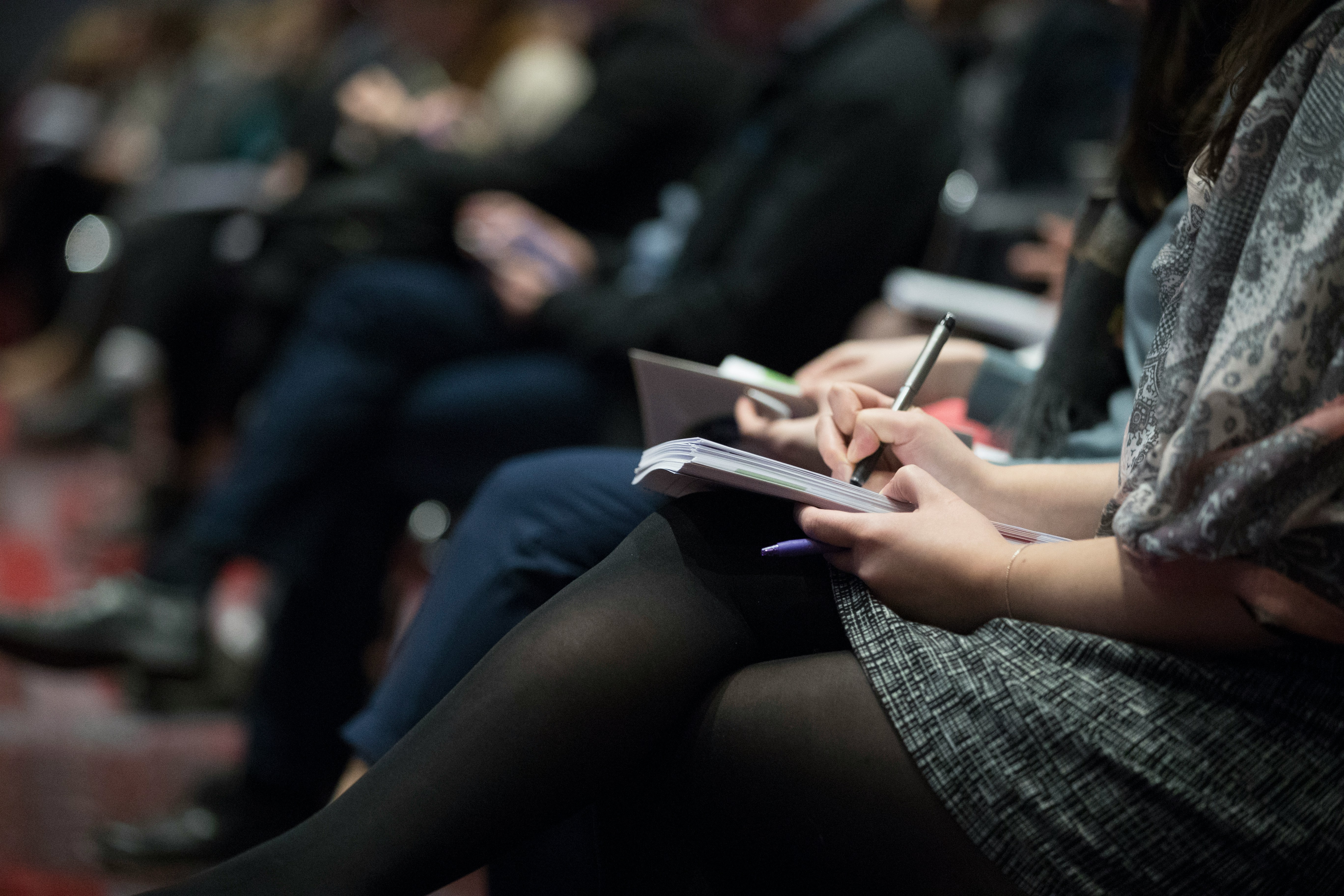A picture of a woman sitting writing notes in a lecture hall